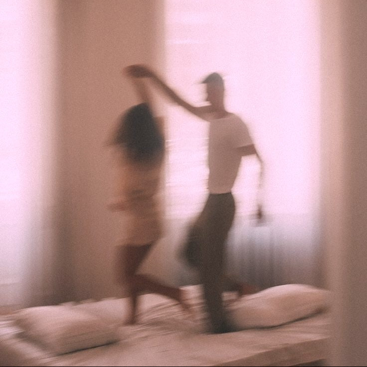 Two people dancing on a bed in a softly lit room.