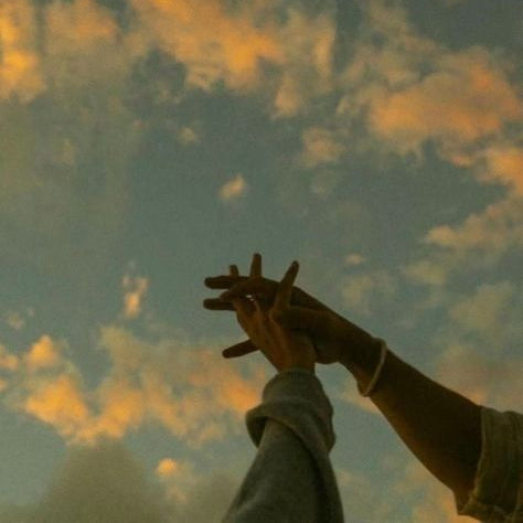 Two hands making a heart shape against a sunset sky.