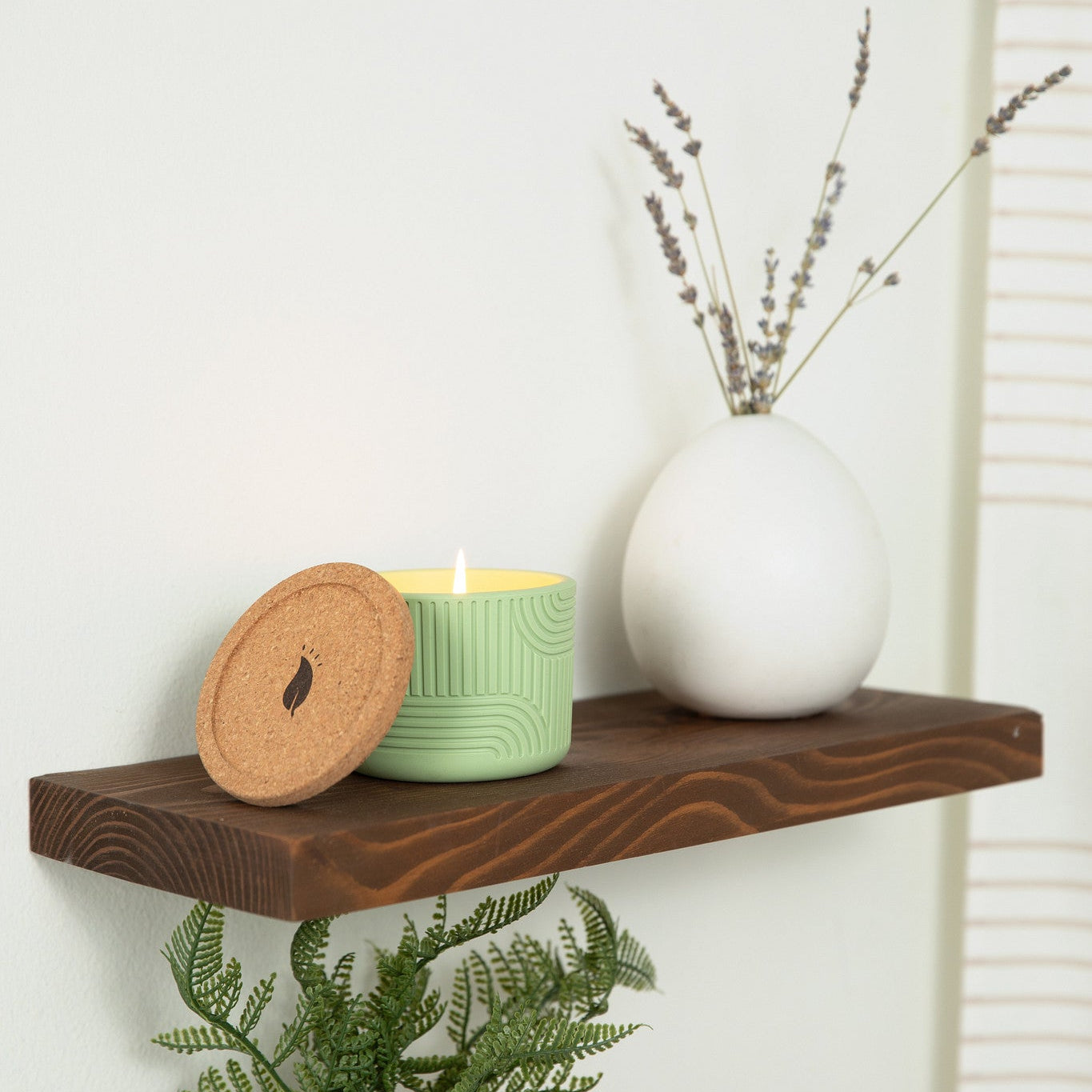 Wooden shelf with decorative items including a plant, candle, and vase against a white wall.